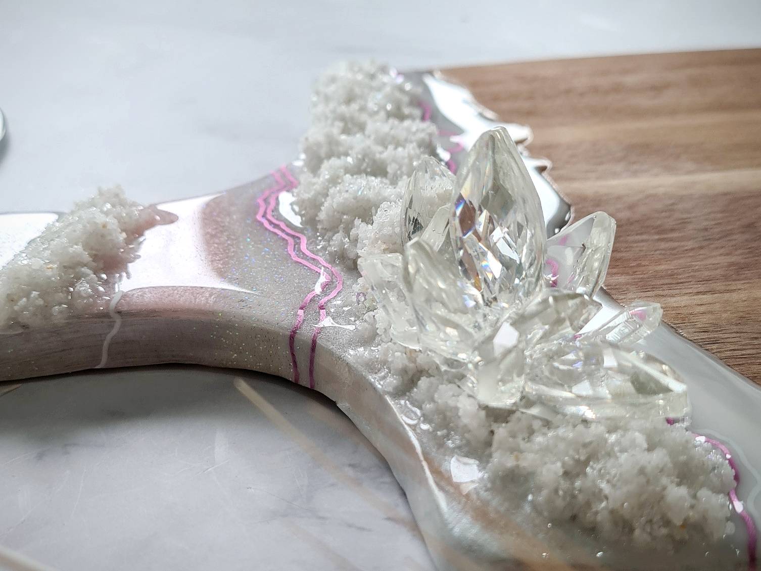 Resin op een houten serveerplank in de kleur wit en roze met transparante resin kristallen erop verwerkt