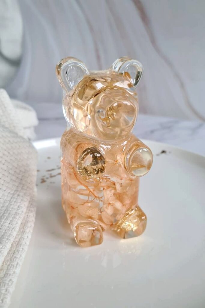 Transparant resin art statue shaped like a gummy bear with dried pink flowers and golden flakes