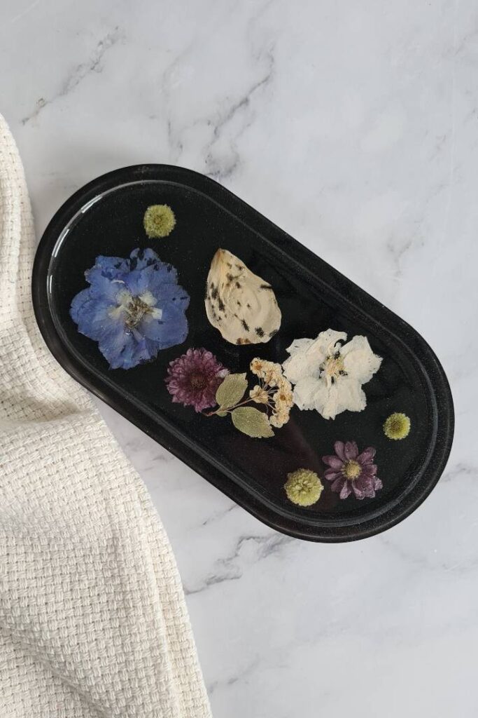 Oval trinket tray made from black epoxy with various colored flowers in it